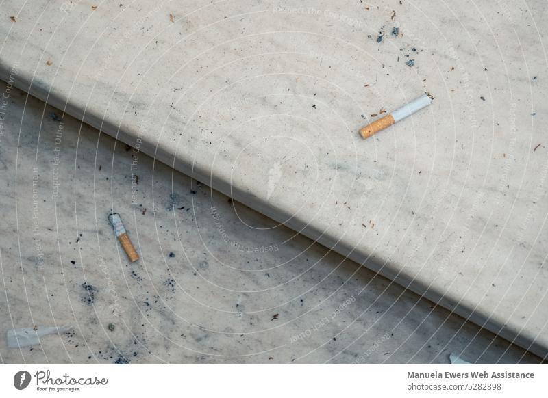 Nahaufnahme von auf einer Treppe herumliegenden Zigaretten in einem heruntergekommenen Einkaufszentrum zigaretten sucht drogen nikotin müll abfall verschmutzt