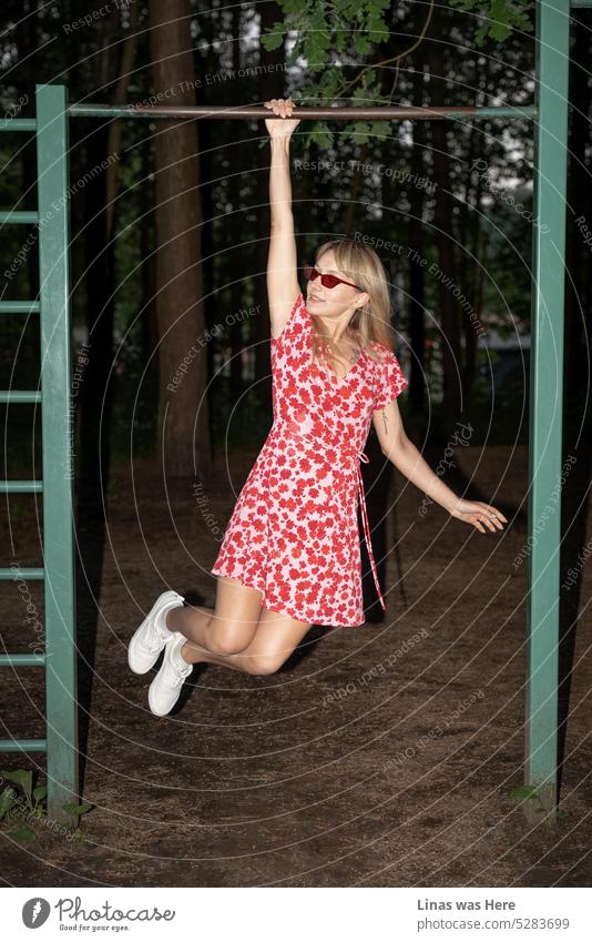 Ein wunderschönes blondes Mädchen in einem roten Sommerkleid macht Sport im Wald. Weiße Schuhe, rote Sonnenbrille und schön gebräunte Beine. Ein Modelltest dieser Schönheit im Wald. Und es ist ein heißer Sommerabend, zweifellos.