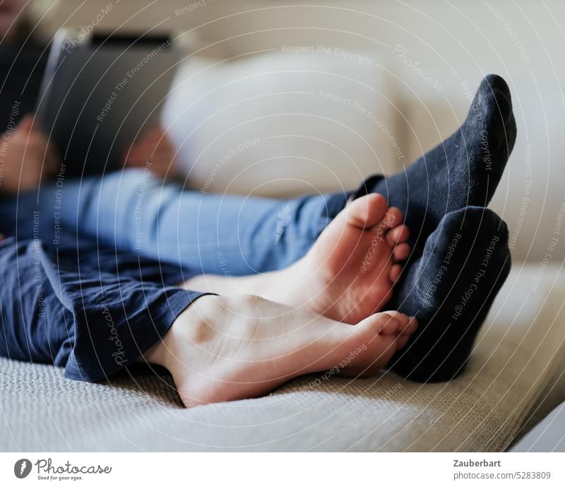 Füße zweier Kinder, barfuß und mit Socken, mit Tablet auf dem Sofa Beine liegen ausruhen spielen daddeln gemütlich Kindheit Erholung Füße hoch hochlegen