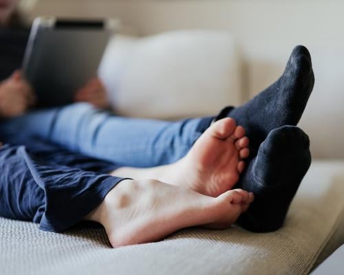Füße zweier Kinder, barfuß und mit Socken, mit Tablet auf dem Sofa Beine liegen ausruhen spielen daddeln gemütlich Kindheit Erholung Füße hoch hochlegen
