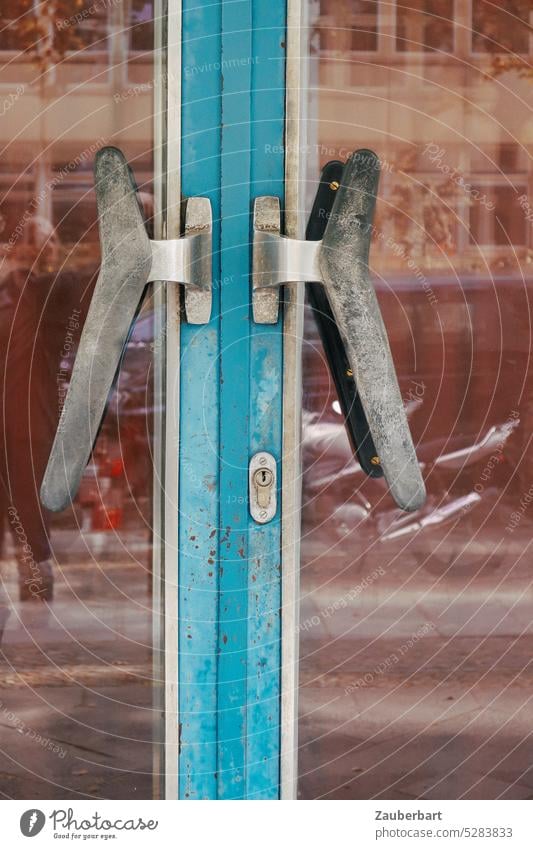 Türgriffe an blauer Stahltür der 60er Jahre, spiegelnde Scheiben zeigen Großstadt mit Fassade und Motorrad Griff Eingang Spiegelung Stadt urban Urbanität