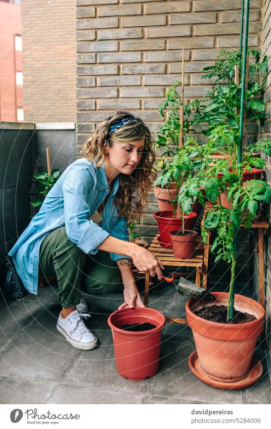 Frau benutzt eine Schaufel, um einen Pflanzentopf im städtischen Garten auf der Terrasse mit Erde zu füllen Gärtner Werfen Verguss besetzen Boden Topf urban