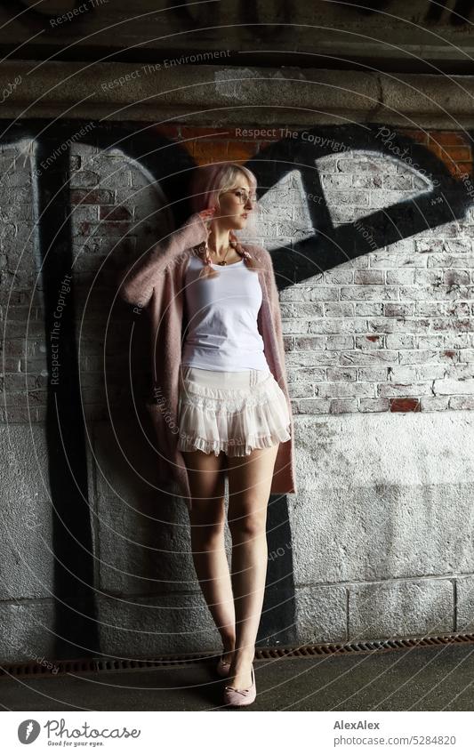 Junge Frau mit pink-blonden Haaren steht vor einer Backsteinwand in einem Tunnel mit Graffiti junge Frau Wand Portrait Brille schön schlank lange Haare