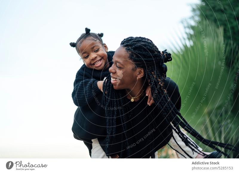 Glückliche schwarze Mutter, die ihre Tochter huckepack nimmt Frau Mädchen Huckepack Mitfahrgelegenheit Spaß haben tropisch Kindheit Wochenende Lächeln heiter