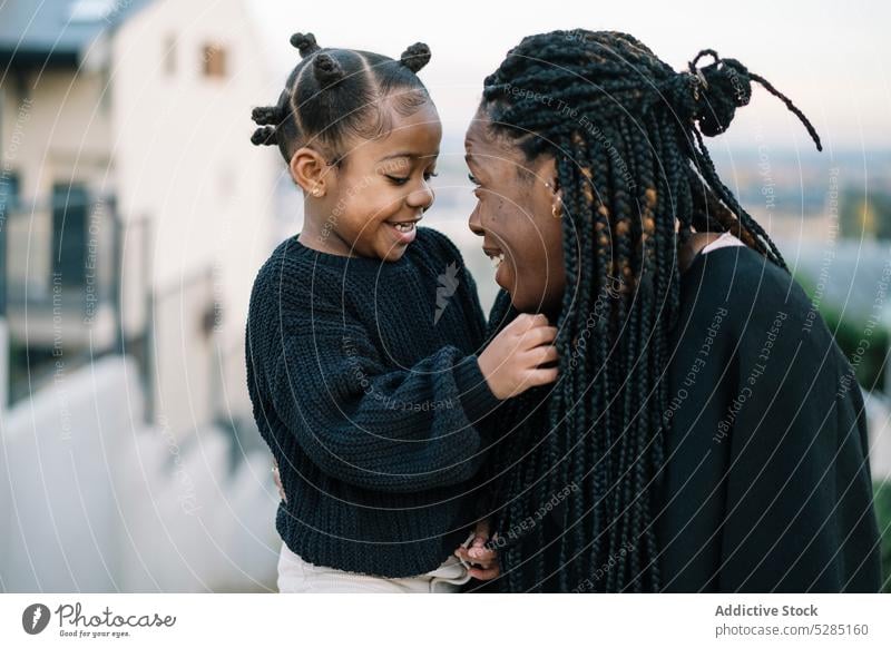 Glückliche schwarze Mutter und Tochter umarmen sich im Freien Frau Mädchen Streichholz abstützen Pflege Bonden Lächeln Straße Angebot kuscheln Kind