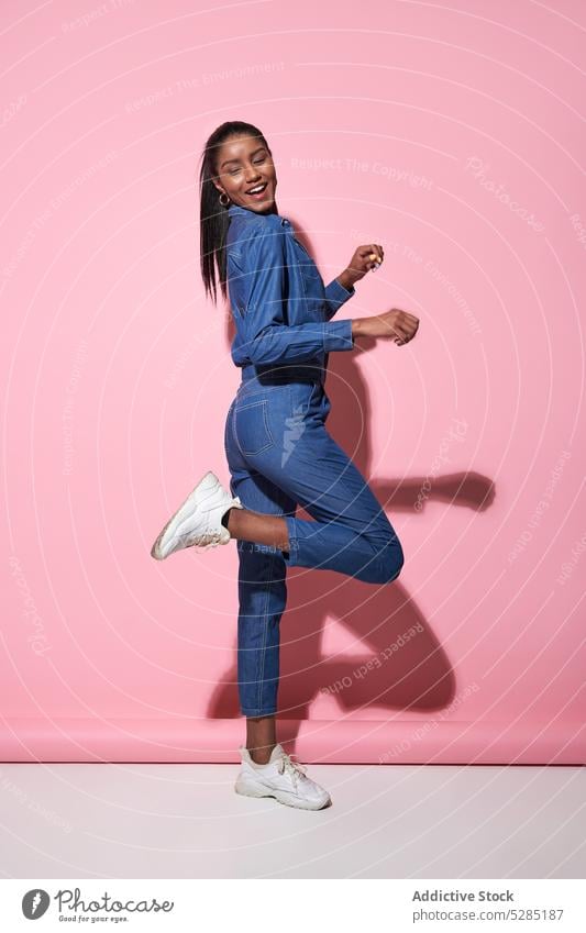 Aufgeregte schwarze Frau springt im Studio Model springen Stil trendy Glück Outfit aufgeregt heiter jung Afroamerikaner ethnisch positiv Lächeln Freude