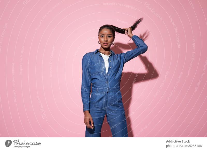Stilvolle schwarze Frau, die während eines Fototermins ihr Haar berührt selbstbewusst Haare berühren Model trendy Jeansstoff Anzug Outfit jung Afroamerikaner