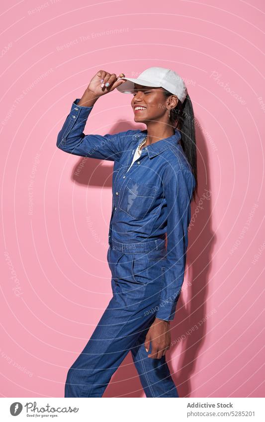 Glückliche stilvolle schwarze Frau mit weißer Mütze im Studio Stil Jeansstoff Mode trendy Outfit Model heiter Bekleidung Lächeln Vorschein Jeanshose