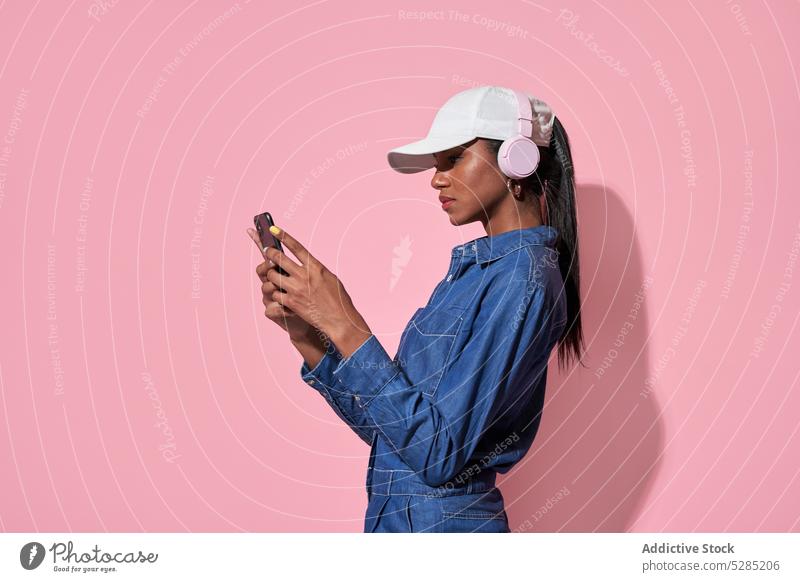 Seriöse schwarze Frau mit Kopfhörern, die auf ihrem Smartphone Nachrichten schreibt Surfen Browsen zuhören Internet Mode selbstbewusst ernst Stil Afroamerikaner