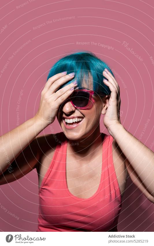 Fröhliche junge Frau mit blauem Haar auf rosa Hintergrund Tastkopf Studioaufnahme Sonnenbrille Freude genießen sorgenfrei Haare berühren Individualität