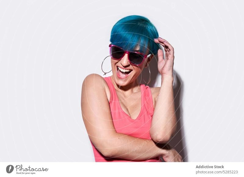 Fröhliche Frau mit blauem Haar im Studio aufgeregt Spaß haben aktiv Sonnenbrille Studioaufnahme heiter einzigartig Freude Brille Lächeln positiv Glück jung