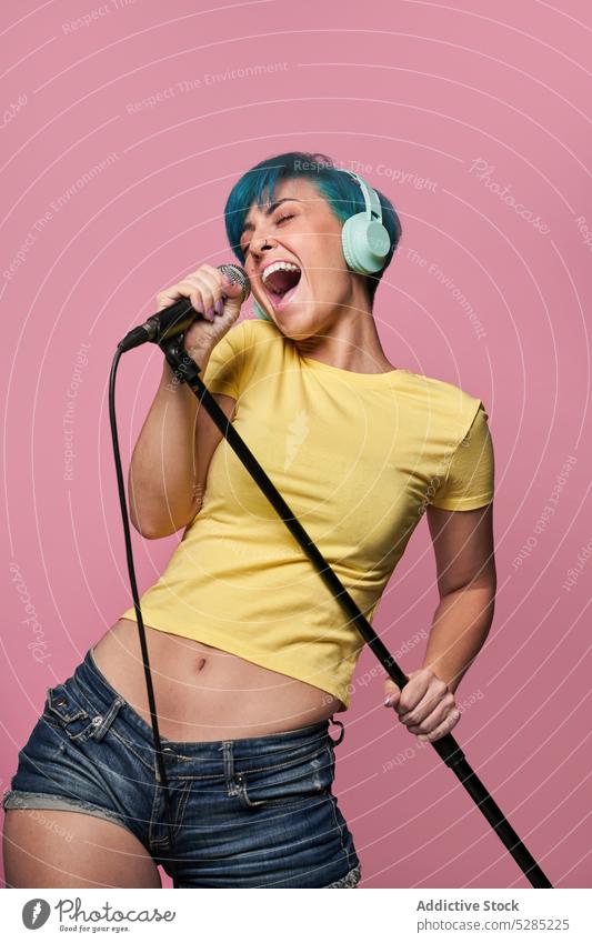 Fröhliche Frau mit Kopfhörern, die in ein Mikrofon singt singen Gesang zuhören Musik unterhalten Stimme aktiv heiter Spaß Freude expressiv jung Klang Audio