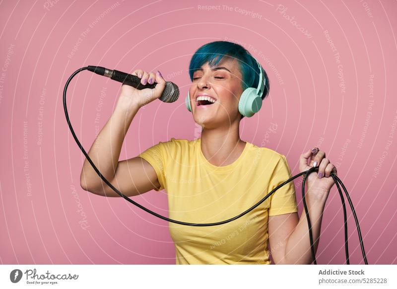 Fröhliche Frau mit Kopfhörern, die in ein Mikrofon singt singen Gesang zuhören Musik unterhalten Stimme aktiv heiter Spaß Freude expressiv jung Klang Audio