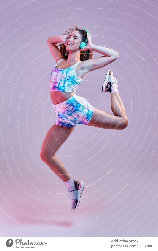 Springende Frau beim Hören von Musik über Kopfhörer Tanzen springen Energie Bewegung berühren Studioaufnahme zuhören meloman Melodie Klang jung