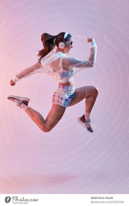 Fitte Frau in Sportkleidung und Kopfhörern springt auf Athlet Stil Sportbekleidung Energie springen aktiv Fitness zuhören Musik Training Glück farbenfroh