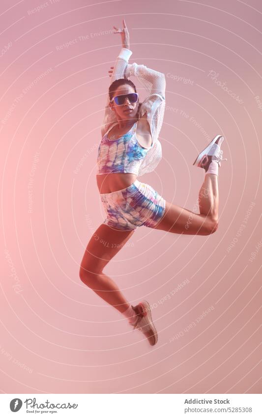 Fitte Frau springt im Studio Tanzen springen Energie Arme hochgezogen sich[Akk] bewegen aktiv Studioaufnahme Sonnenbrille passen sportlich perfekt Körper jung