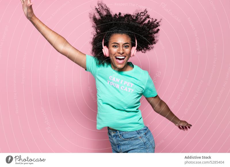 Aufgeregte schwarze Frau springt und lächelt Musik springen zuhören Glück Kopfhörer Energie Lächeln Stil farbenfroh jung Afroamerikaner ethnisch Freude heiter