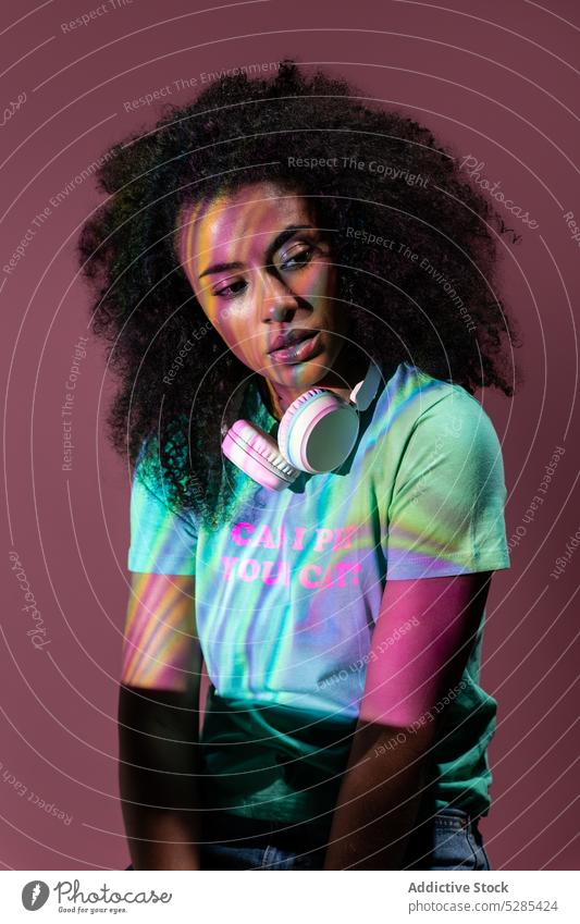 Nachdenkliche schwarze Frau mit Kopfhörern in Neonfarben neonfarbig besinnlich nachdenklich trendy Licht ernst Reflexion & Spiegelung Stil jung ethnisch