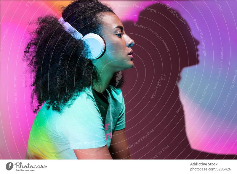 Nachdenkliche schwarze Frau hört Musik in Neonfarben Kopfhörer zuhören meloman neonfarbig verträumt Afro-Look Gesang Wiedergabeliste Drahtlos Licht besinnlich