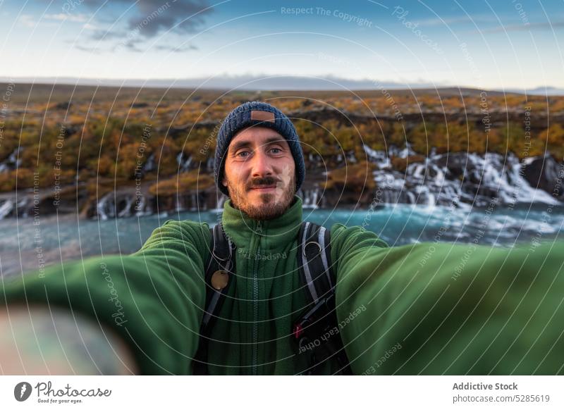 Positiv eingestellter Reisender macht Selfie in der Nähe eines Wasserfalls Mann Wanderer Tourist Selbstportrait Kaskade Herbst Berge u. Gebirge Natur Island
