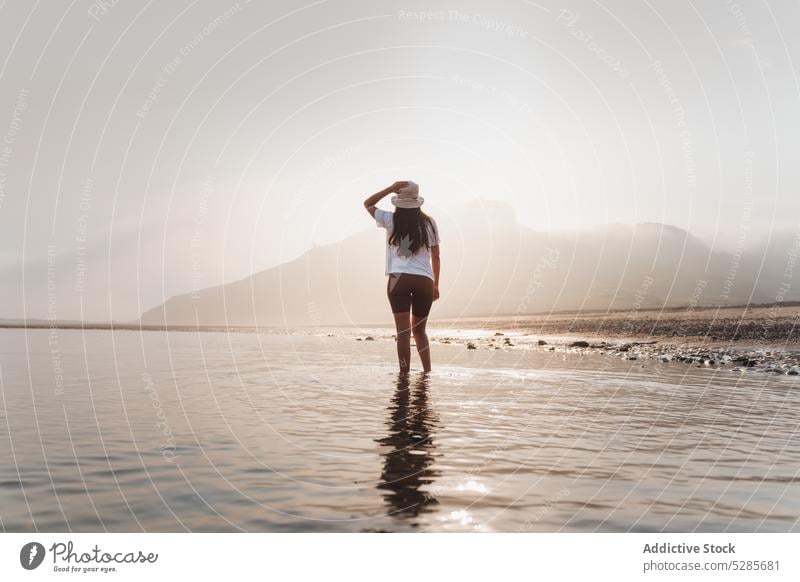 Anonyme Frau, die im Meerwasser in der Nähe eines Berges spazieren geht Tourist Spaziergang MEER Ufer Strand Sommer Berge u. Gebirge Urlaub Natur Küste Wasser