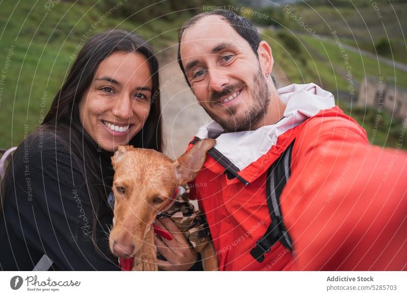 Glückliches Paar macht Selfie mit Hund auf der Straße Lächeln Tourist Haustier fotografieren Weg Hochland Zusammensein Partnerschaft Umarmung Natur heiter