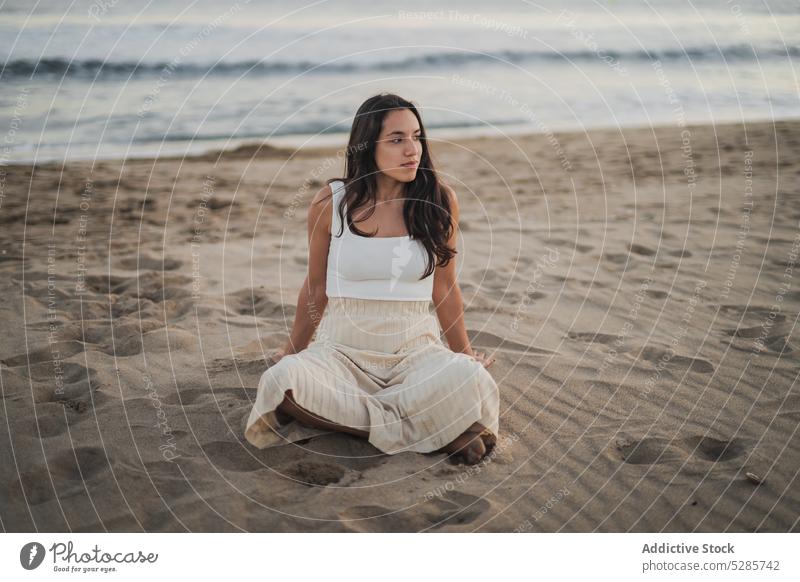 Entspannte junge hispanische Frau sitzt mit gekreuzten Beinen am sandigen Meeresstrand Strand ruhen Feiertag Tourist Urlaub Beine gekreuzt Erholung MEER allein