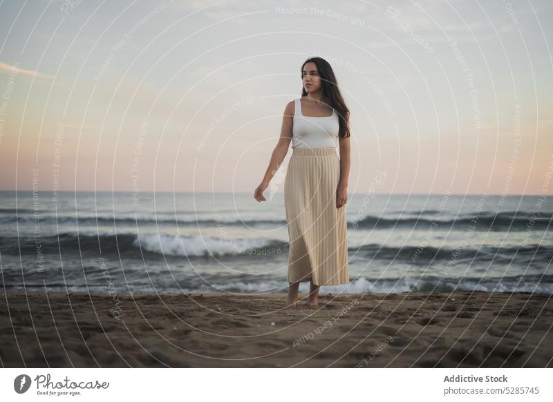 Fröhliche junge ethnische Frau, die im Sommerurlaub am sandigen Meeresufer steht Spaziergang Strand MEER genießen Feiertag Sonnenuntergang Reisender Sand Natur