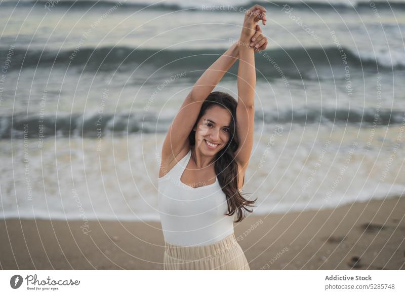 Zufriedene junge hispanische Frau tanzt am Sandstrand Tanzen Strand Sonnenuntergang Arme hochgezogen positiv MEER ausführen selbstbewusst feminin sorgenfrei