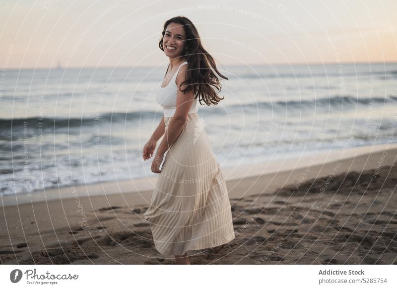 Fröhliche junge ethnische Frau, die während des Sommerurlaubs am sandigen Meeresufer spazieren geht Spaziergang Strand Lächeln MEER genießen Glück Feiertag
