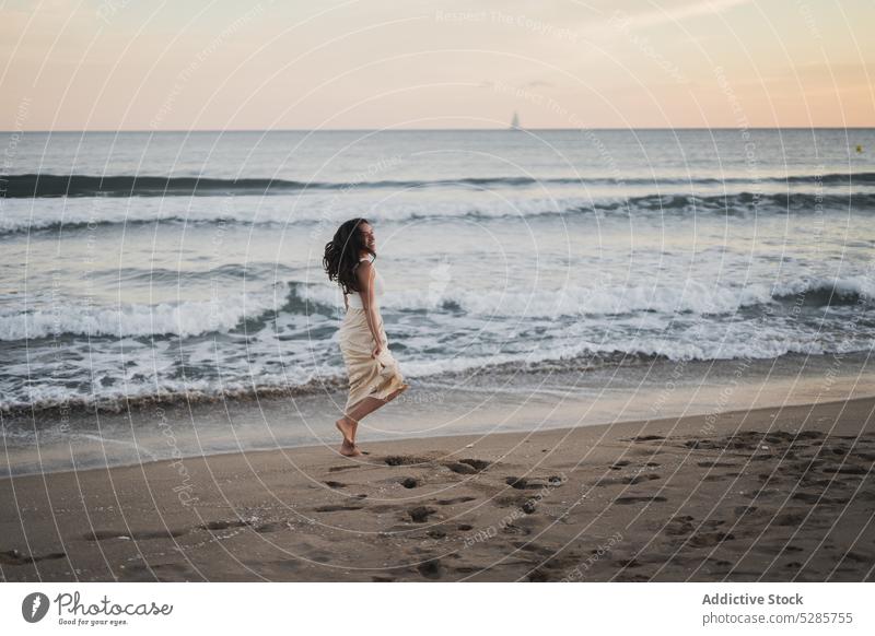 Fröhliche junge ethnische Frau, die während des Sommerurlaubs am sandigen Meeresufer spazieren geht Spaziergang Strand Lächeln MEER genießen Glück Feiertag