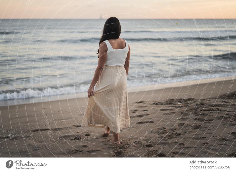Anonyme junge ethnische Frau, die im Sommerurlaub am sandigen Meeresufer steht Spaziergang Strand MEER genießen Glück Feiertag Sonnenuntergang Reisender Sand