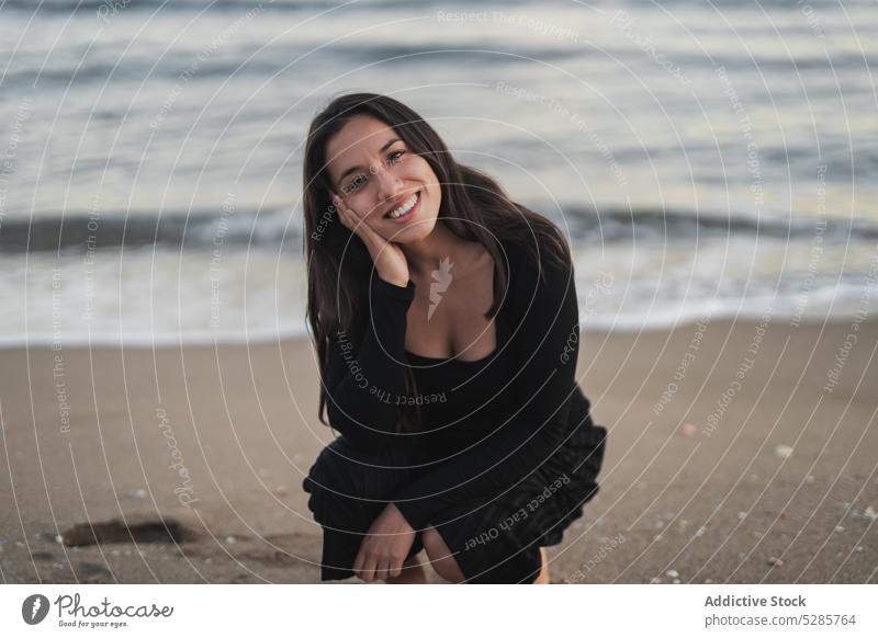 Zufriedene junge ethnische Touristin, die lächelnd am Strand sitzt Frau selbstsicher Urlaub Feiertag feminin MEER ruhen Lächeln Wange berühren Porträt Stil