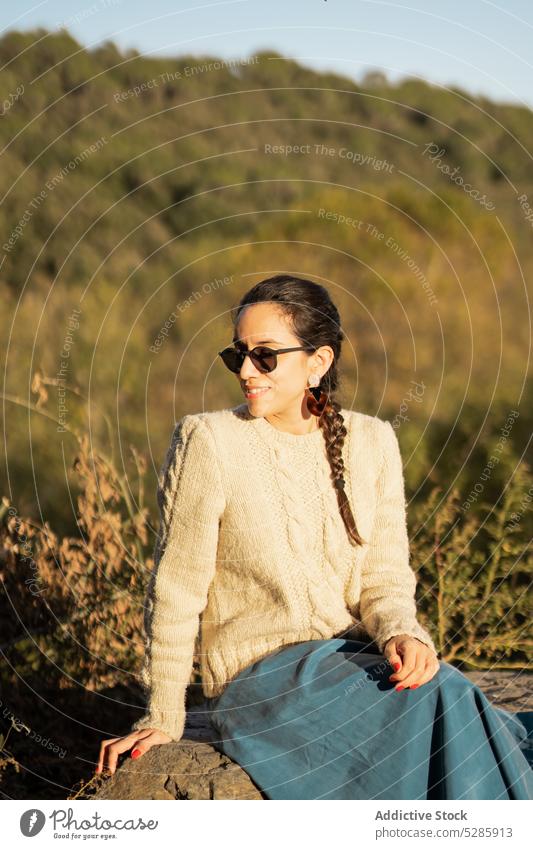 Entspannte Frau auf Stein ruhend trendy Landschaft sich[Akk] entspannen positiv Stil Lächeln Natur ländlich jung ethnisch Sommer Sonnenbrille heiter Glück