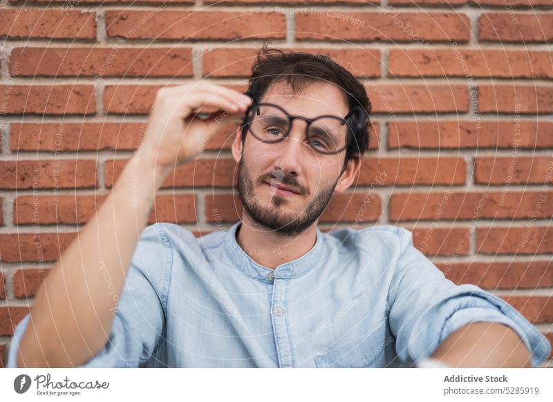 Nachdenklicher Mann mit Brille an einer Backsteinmauer besinnlich nachdenklich Backsteinwand Hipster selbstbewusst Vollbart ernst sitzen lässig männlich Denken
