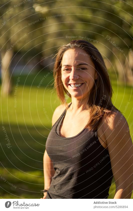 Fröhliche, sportliche Frau im sonnigen Park Athlet heiter Porträt Lächeln Sportbekleidung Sommer Training Fitness positiv Wohlbefinden Sportlerin selbstbewusst