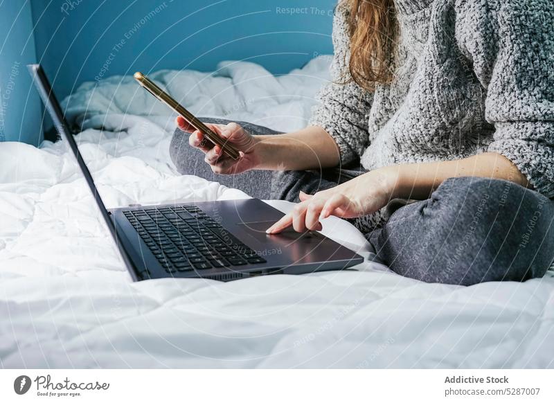Crop-Frau surft auf dem Bett mit Laptop und Smartphone benutzend Funktelefon Touchpad freiberuflich selbständig Browsen unabhängig Talkrunde Projekt Apparatur