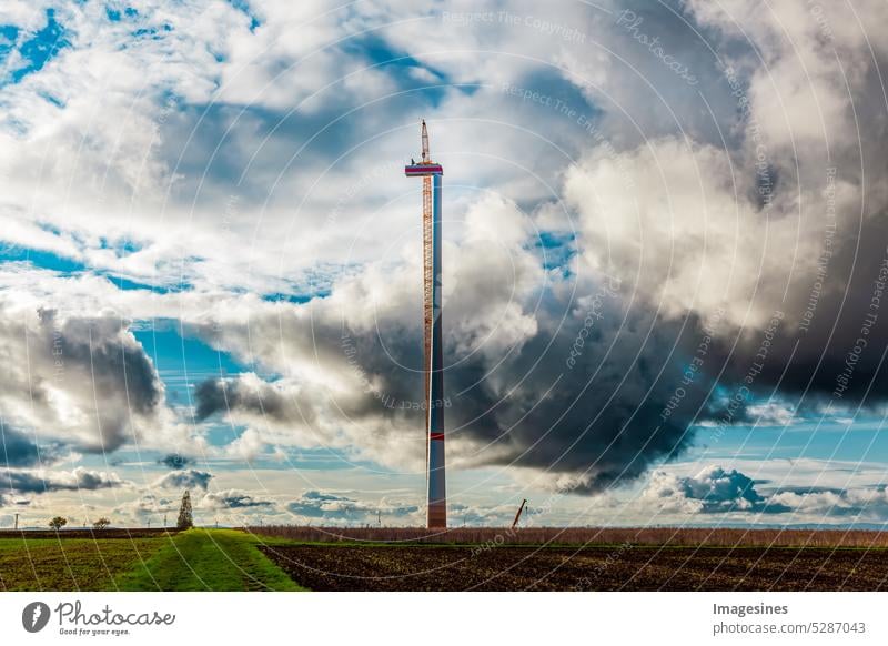 Unwetter. Bau und Montage einer Windkraftanlage per Kran und dunkle Wolken ziehen auf, Ackerland mit Bauarbeiten für Windkraftanlagen im Windpark. Gewitterwolken ziehen auf. Wörrstadt, Deutschland.