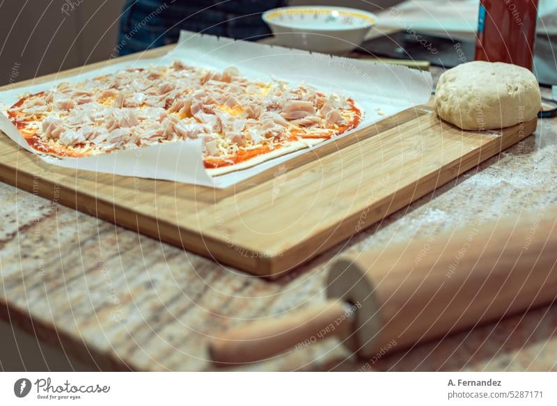 Eine hausgemachte Schinken-Käse-Pizza auf einem Holzbrett neben einem Nudelholz. Konzept der Zubereitung von Pizzen zu Hause hausgemachte Speisen