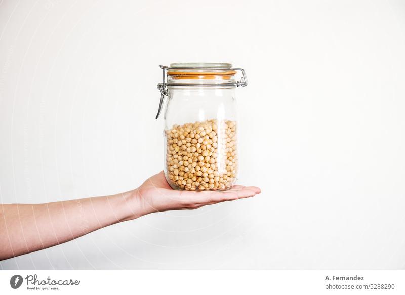 Detail einer Hand, die ein Glas mit Kichererbsen hält. Konzept der nachhaltigen Lebensmittelaufbewahrung im heimischen Schrank. Glasgefäß Einmachglas