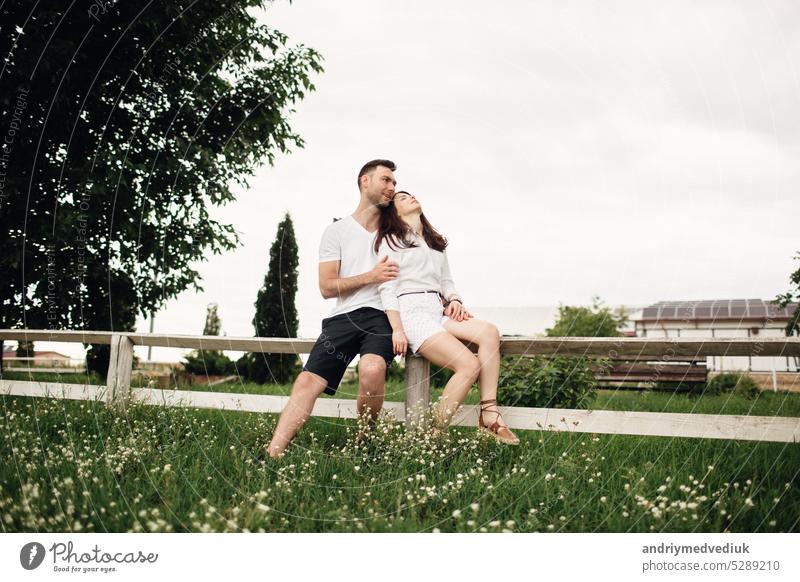 Loving Paar sitzt im Sommer Park auf weißen Zaun. Mann und Frau umarmen im Freien auf warmen Tag Erwachsener jung zwei Zusammensein romantisch Partnerschaft