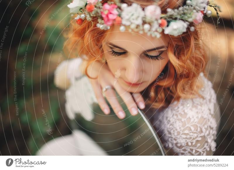schöne junge rothaarige Braut im Wald mit Blumenkranz auf dem Kopf und Spiegel . Frau in langem weißen Kleid im Freien am Sommertag. Hochzeitstag Wälder