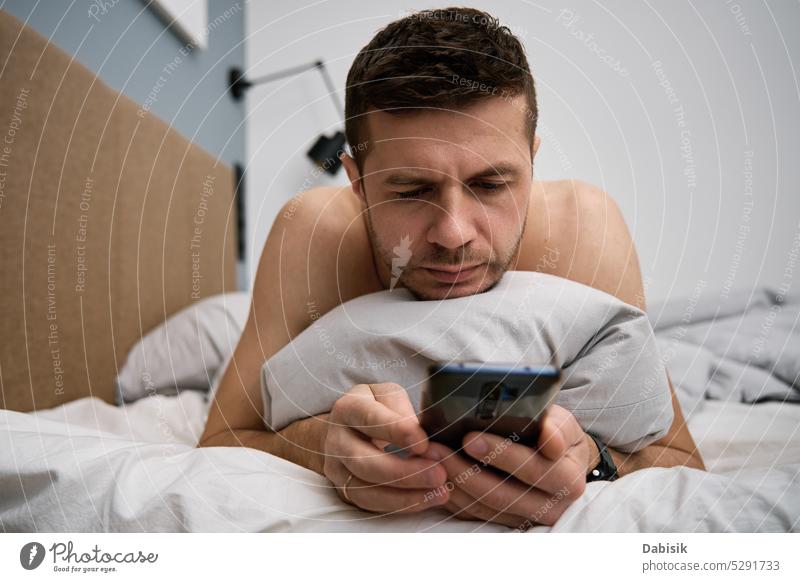 Handy-Sucht. Mann im Bett liegend mit Smartphone Lügen Telefon Schlafzimmer Lifestyle Browsen Morgen Freizeit Funktelefon online aussruhen Decke