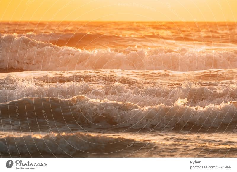 Meerwasseroberfläche bei Sonnenuntergang. Natürliche Sonnenaufgang warmen Farben des Ozeans. Meer Ozean Wasseroberfläche mit schäumenden kleinen Wellen bei Sonnenuntergang. Abend Sonnenlicht Sonnenschein über dem Meer. Amazing Landschaft Landschaft. Natur Hintergrund