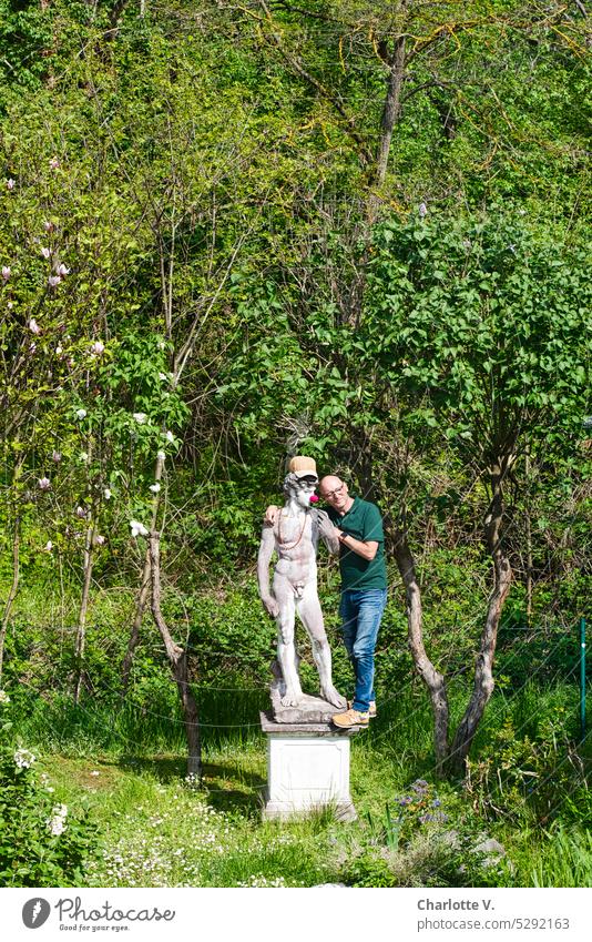 Mainfux I Mensch und Statue David Mann Mann auf Sockel Skulptur Stein Garten Gartenmöblierung historisierend zugewandt Clownsnase Außenaufnahme Arm in Arm Kappe