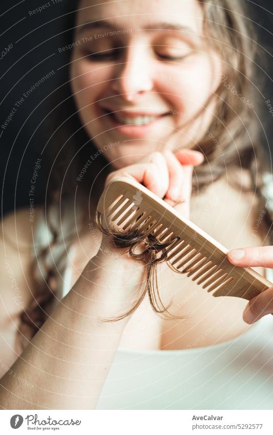 Fröhliche Frau, die ihr Haar mit einem Holzkamm pflegt. Haarsplissbehandlung, tägliche Rutine und Rituale für perfektes und glänzendes langes Haar. Behaarung
