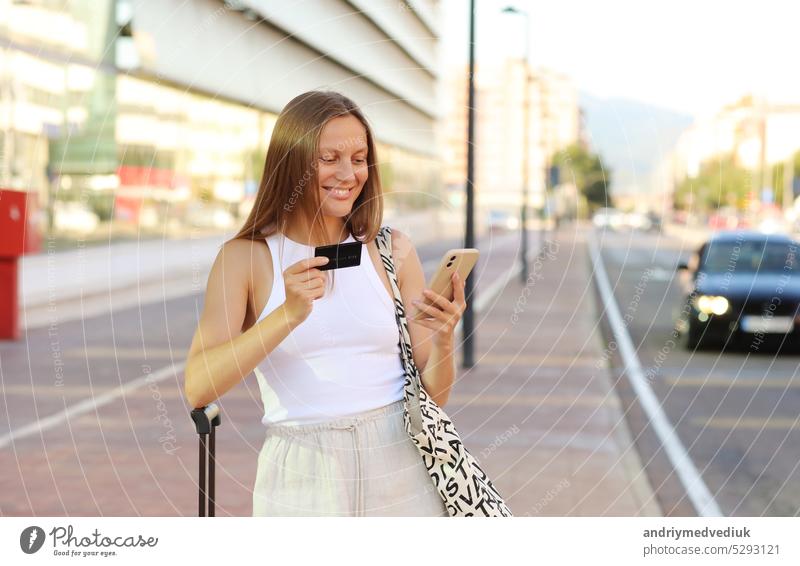 Schöne junge lächelnde Frau mit Smartphone und Kreditkarte durch den Flughafen. Glückliches Mädchen mit Koffer nach angekommen Flugzeug buchen und zahlen für Hotel. Sommerurlaub. neue im Ausland Reise reisen