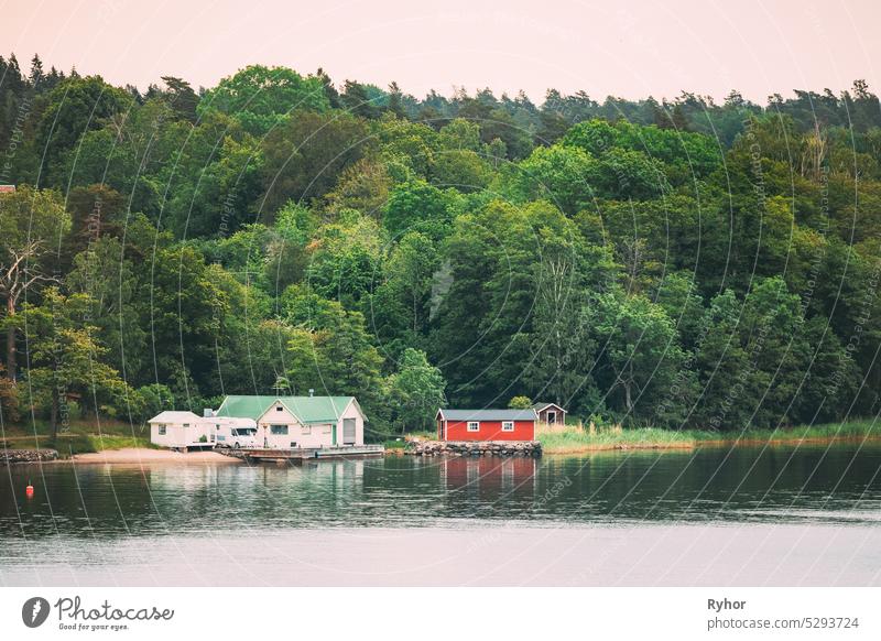 Schweden. Schöne rote schwedische Holzblockhaus Haus auf Rocky Island Küste im Sommer. See oder Fluss und Waldlandschaft Schwedisch Appartement Inselgruppe