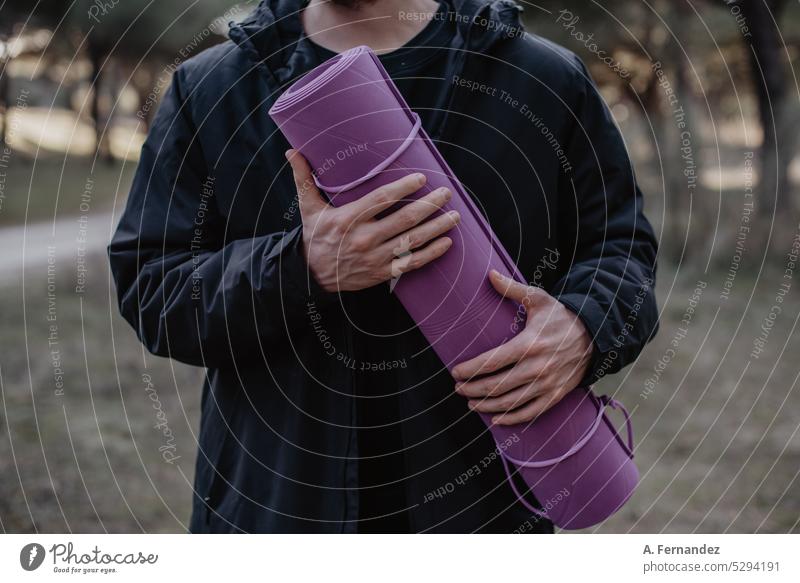 Mann hält eine lila Yogamatte in einem Park. Konzept der Übung im Freien. Mann macht Yoga. Trainingsmatte Unterlage Beteiligung purpur violett Junge außerhalb
