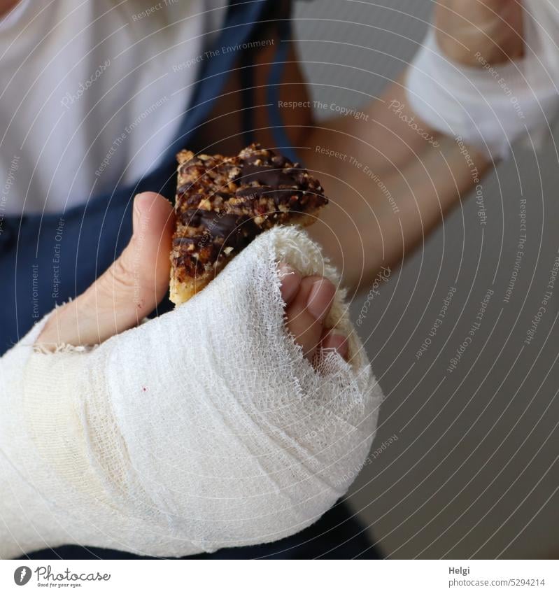 Mainfux-UT | verbundene Hand hält eine Trost-Nussecke Mensch Frau Daumen Finger Arm krank Verband Gips Verletzung halten festhalten essen verletzt Gebäck lecker